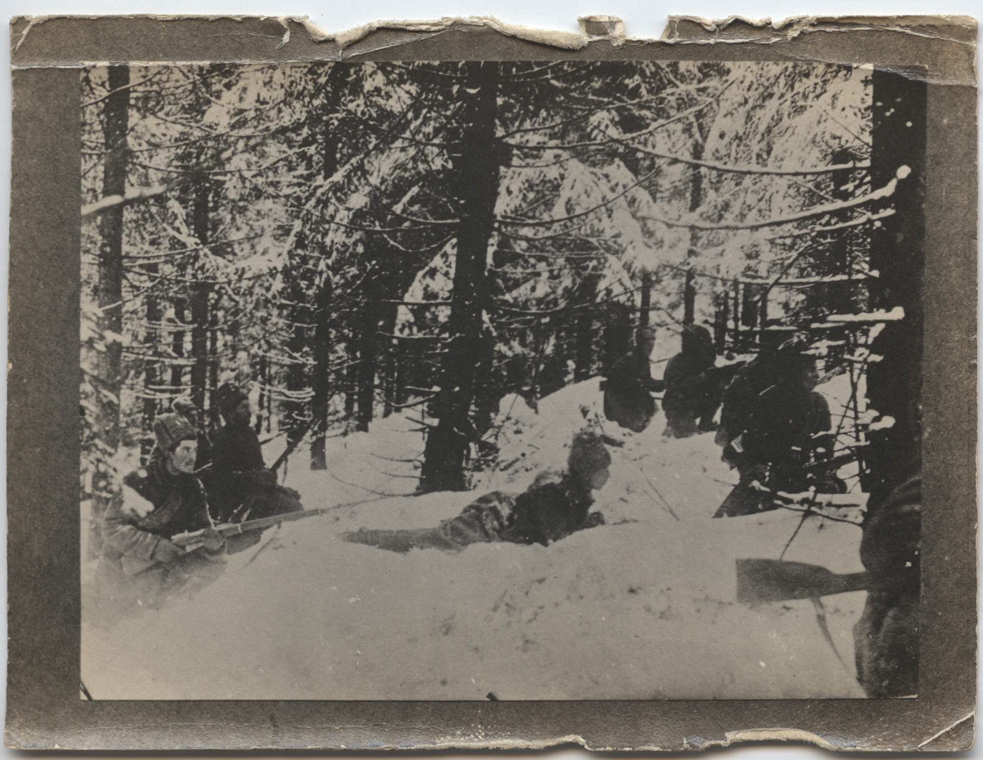 Black and white photograph of soldiers sitting and lying in the snow in a wood, holding firearms
