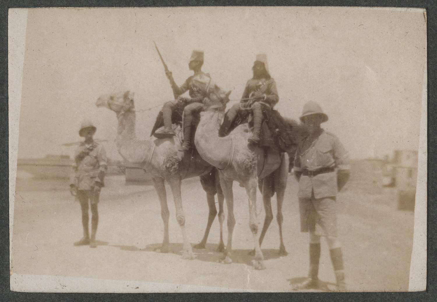 Sepia photograph of two British soldiers posing with two Egyptian soldiers who are riding on camels