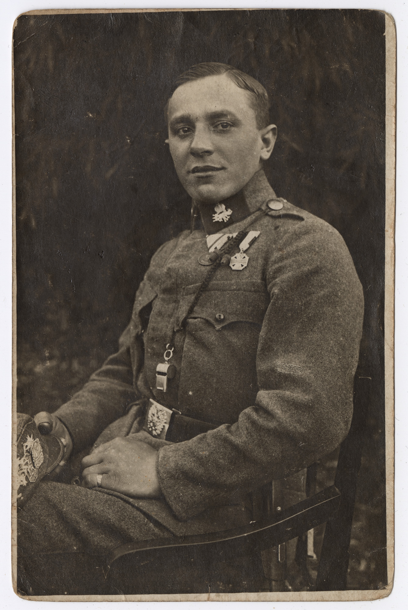 Black and white sitting portrait photograph of a young white man in military uniform wearing a metal whistle around his neck