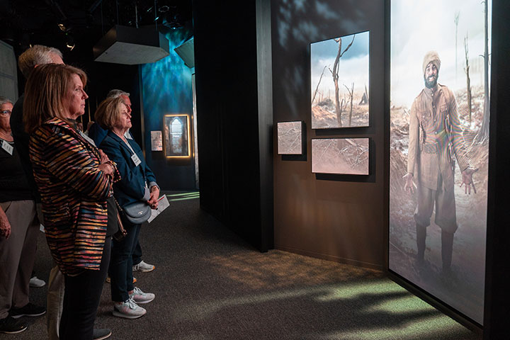 Museum guests watching a video screen depicting an Indian colonial soldier gesturing in despair while standing in a destroyed battlefield