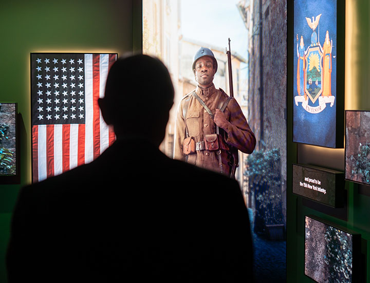Museum visitor watching a large video screen showing a young Black man in WWI uniform in a European city