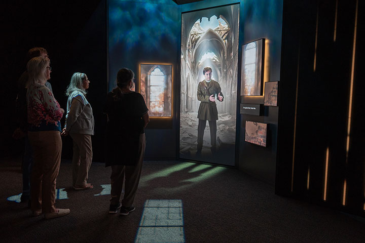 Guests watching a video screen depicting a white soldier standing in a bombed-out cathedral