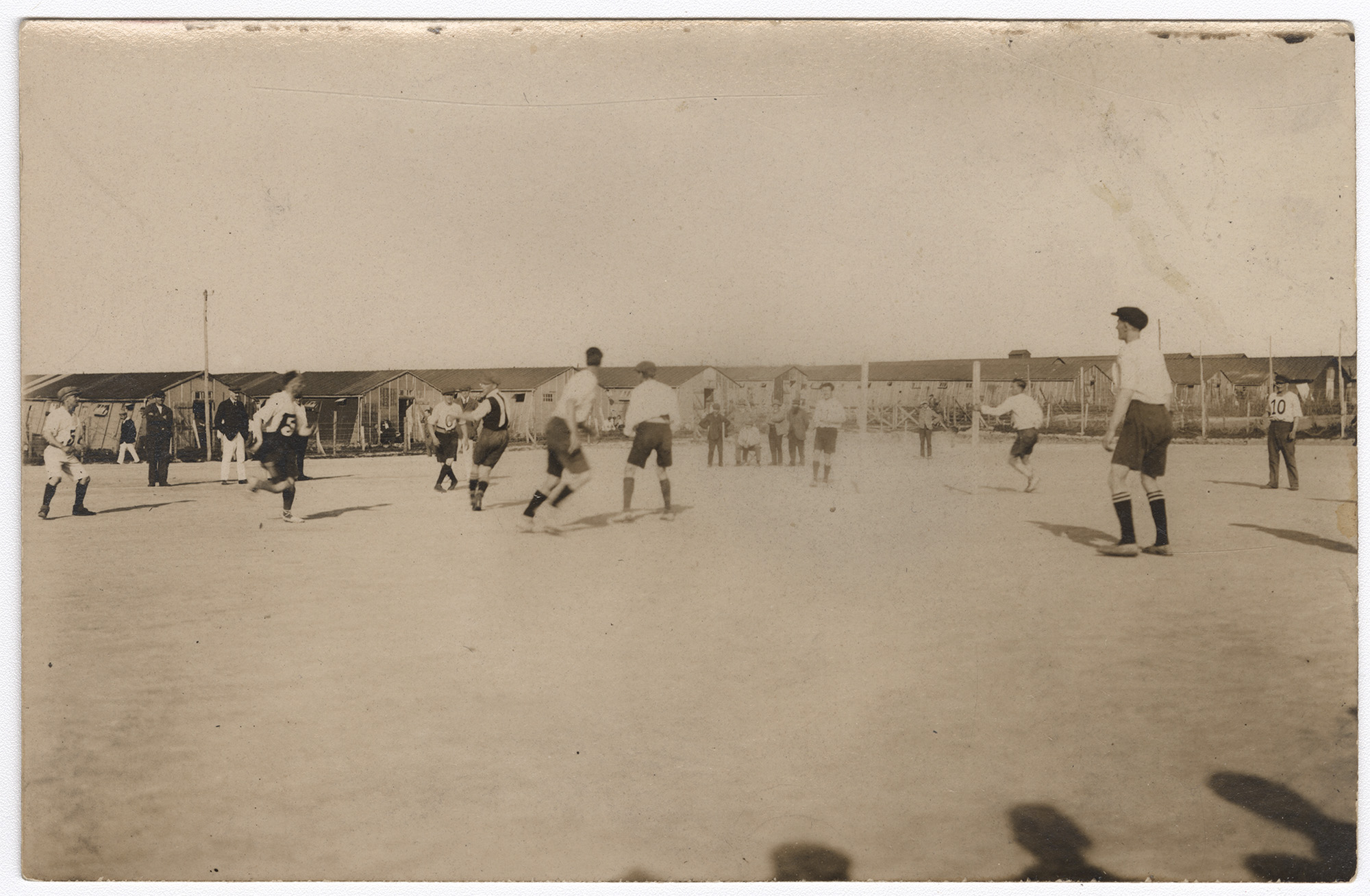 Black and white photo of men playing football on a field with barracks in the background