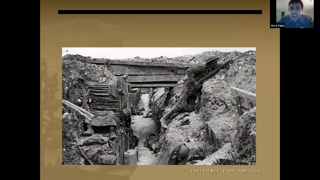 Black and white photo of a WWI soldier peering over the top of a trench with his gun at the ready