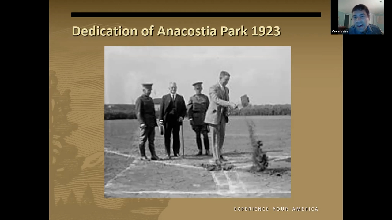 Black and white photo of a white man in a suit standing on a baseball diamond pouring a bucket of dirt onto the ground
