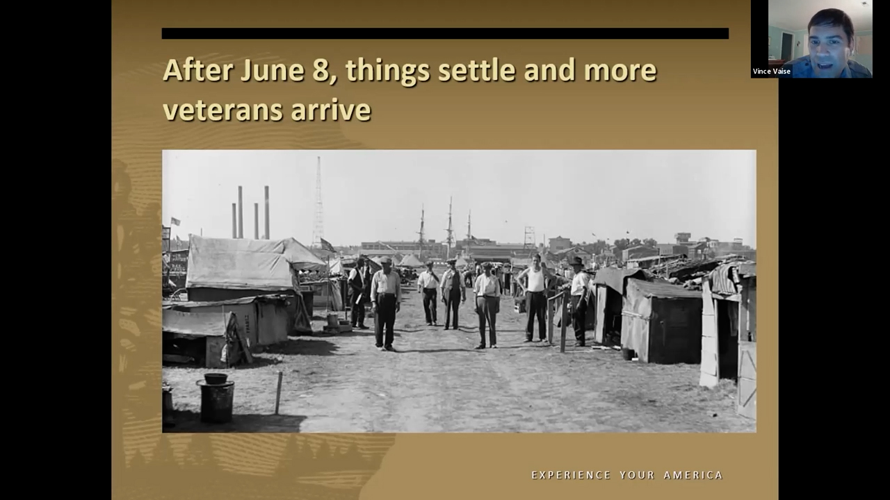 Black and white photo of men walking down a wide street in a shantytown encampment