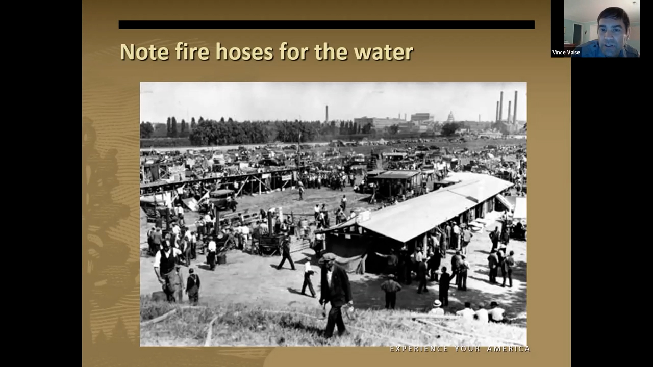 View of the shantytown from a hill. In the foreground, a man stands on the slope of the hill with hoses snaking down the hill.