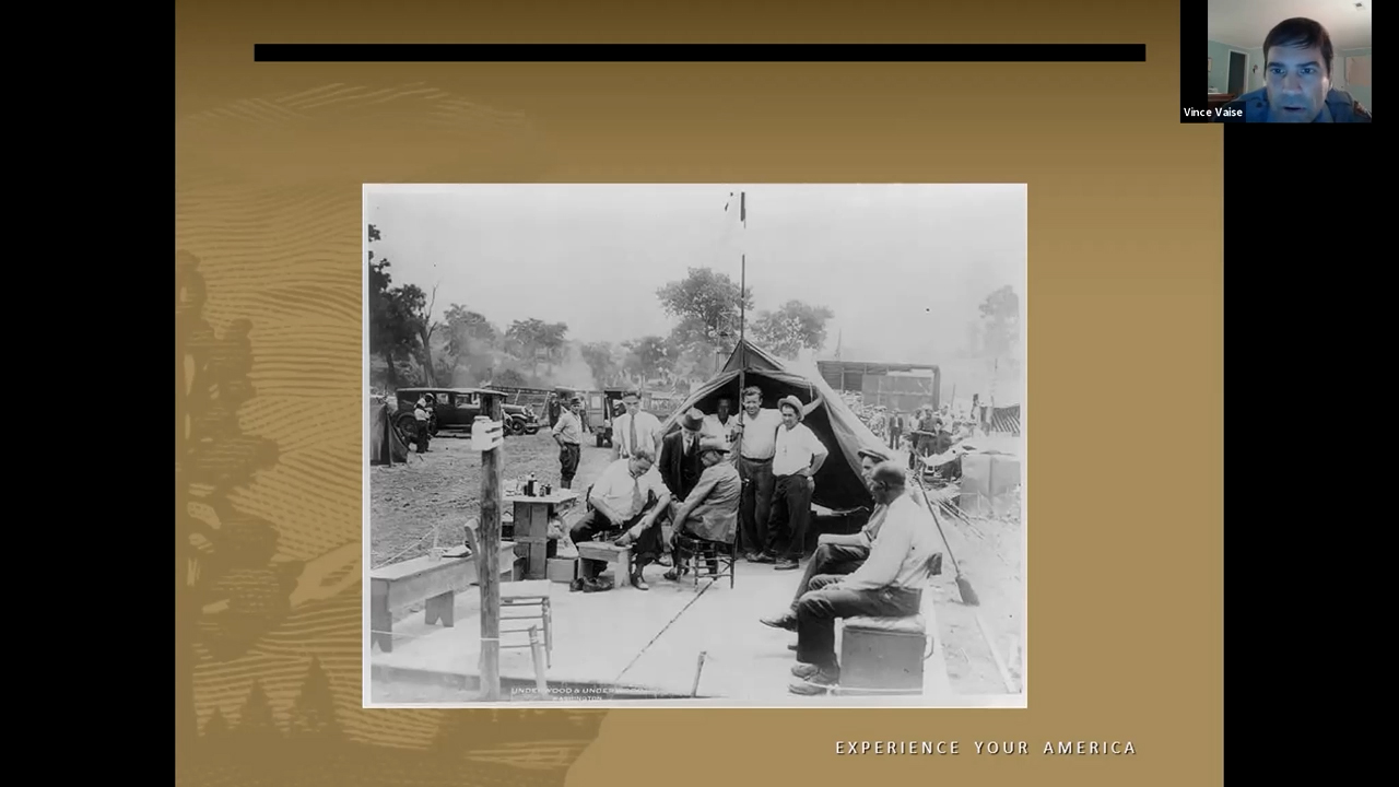 Black and white photo of a group of men gathered around the front of a tent