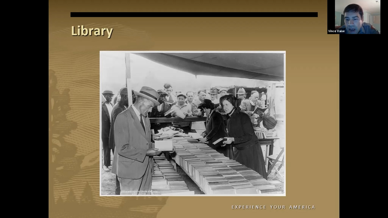 Black and white photo of people crowded around a long table loaded with books