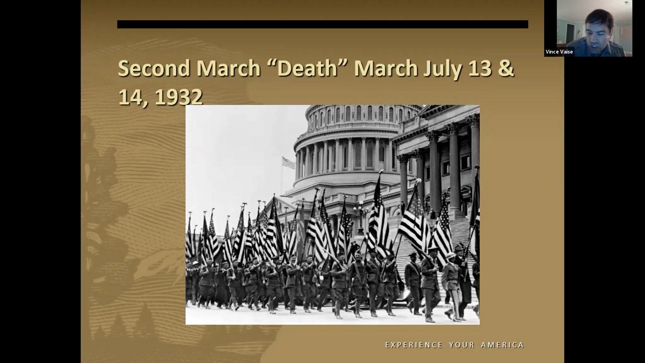Black and white photo of men marching around the Capitol building carrying U.S. flags.