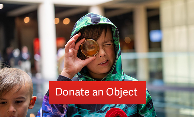 A white boy looks through some kind of historical artifact that is a lens. Text: 'Donate an Object'