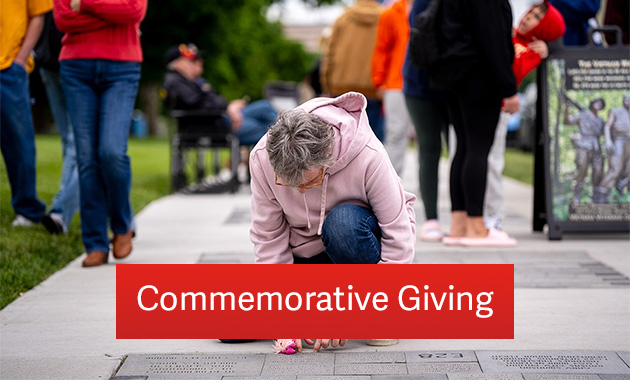 Person wearing a pink sweatshirt and jeans kneeling by a display of engraved bricks embedded in a sidewalk. Text: 'Commemorative Giving'