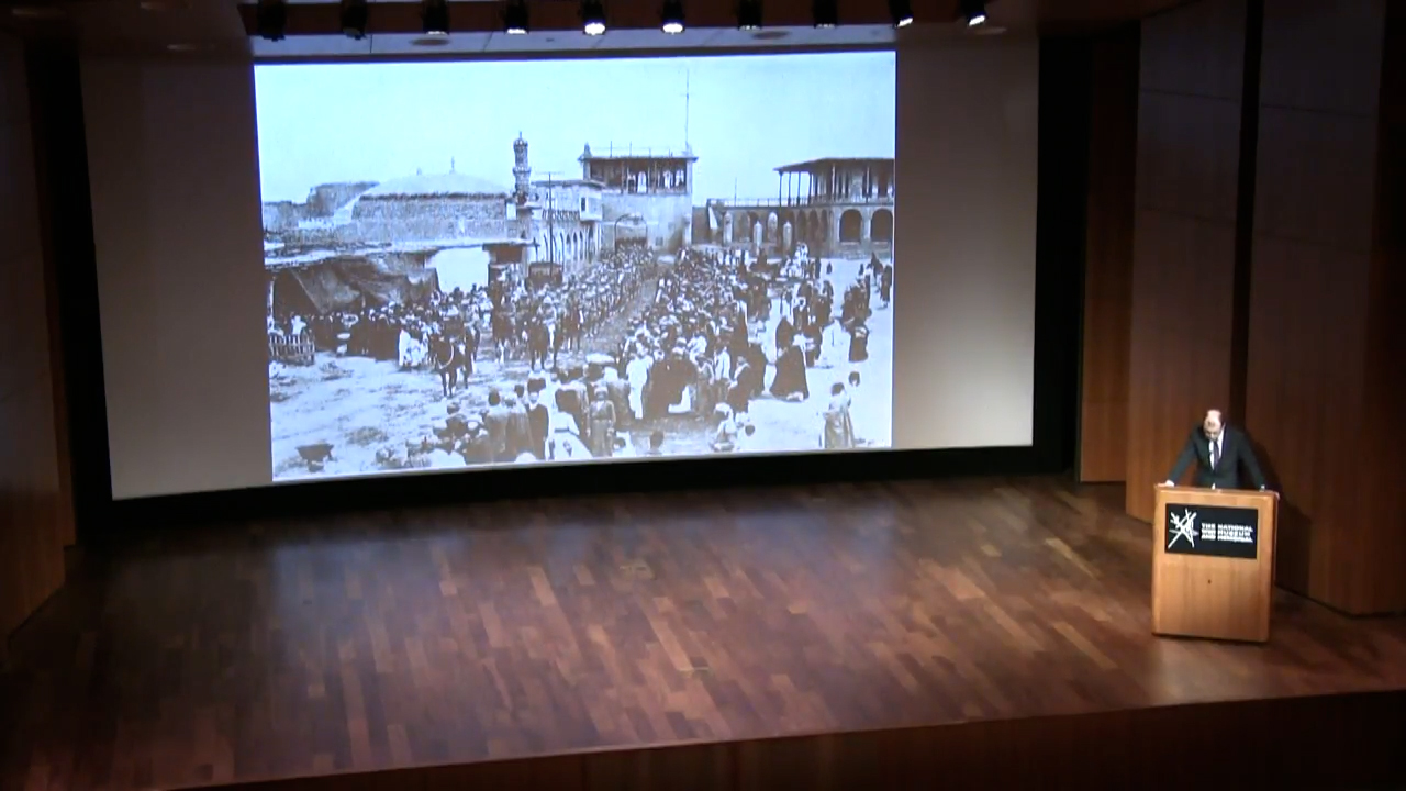 Black and white photo of soldiers marching down a city street while civilians look on
