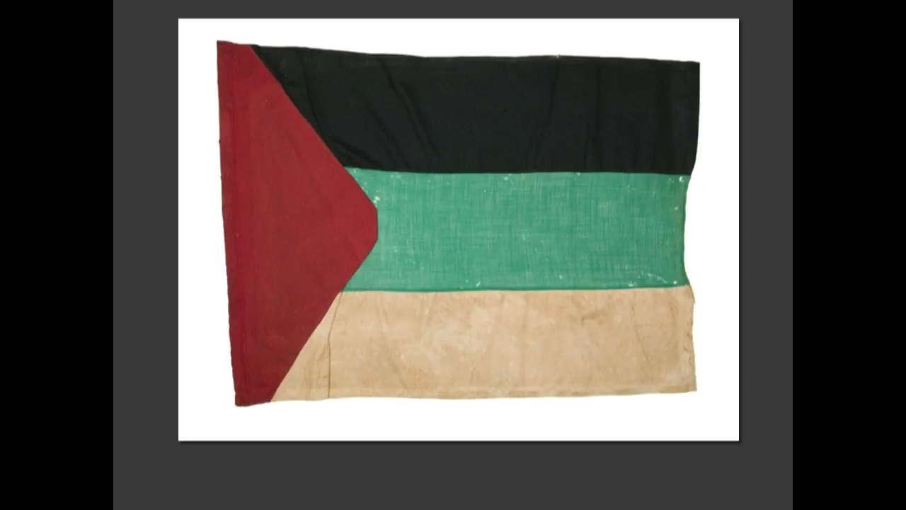 Photograph of a historical flag with black, green, white stripes and a red triangle.