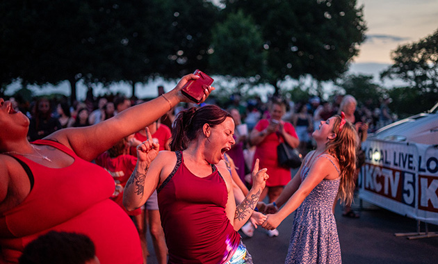 Modern photo of people dancing enthusiastically on the Museum and Memorial grounds. A KCTV5 banner is in the background