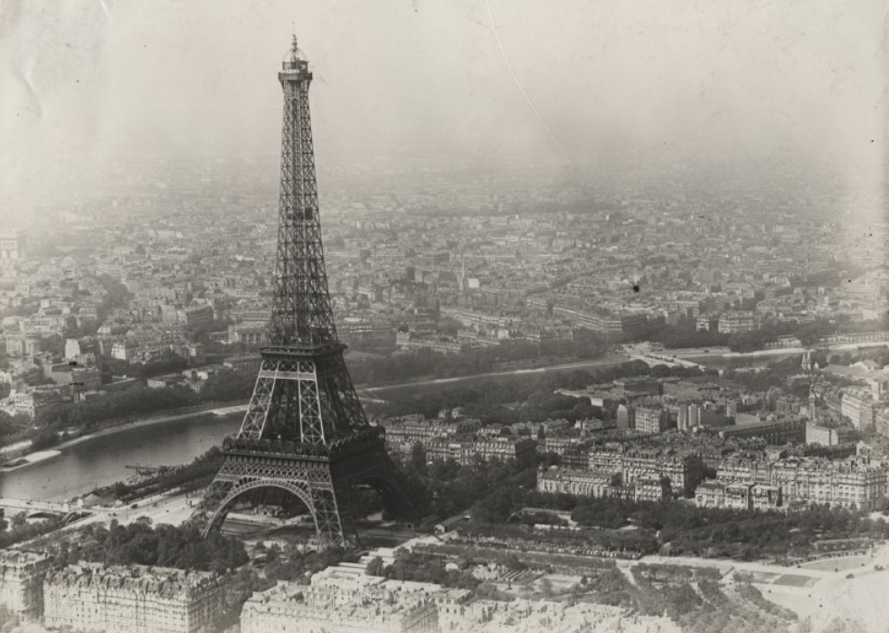 Black and white photograph of the city of Paris from a high point. The photo includes the Eiffel Tower.
