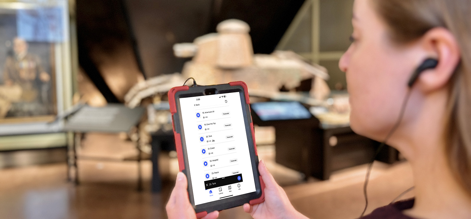 A person in the Main Gallery wearing wired earbuds plugged into a tablet that displays the Audioguide interface