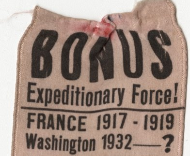 A potion of a tan ribbon with black text on it. The top of the ribbon is frayed. The text says "BONUS Expeditionary Force! / FRANCE 1917 - 1919 / Washington 1932 - ?"