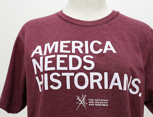 Modern photo of a maroon t-shirt printed with 'America Needs Historians' in all-caps
