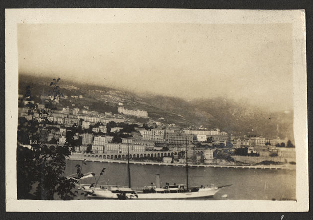 Black and white photo of a harbor or channel with houses in the background and a sailing yacht in the foreground
