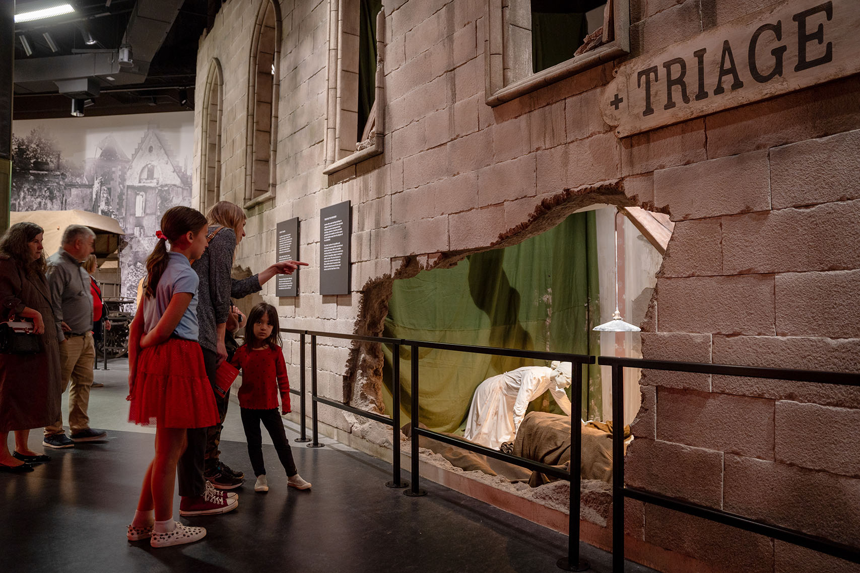 Museum guests look at an exhibit of a bombed-out church with life-size mannequins inside depicting nurses and medics taking care of wounded soldiers
