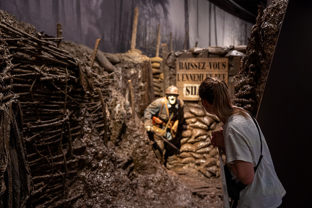 A museum guest leans into a trench display depicting a life-size mannequin of a WWI soldier charging into a trench on the attack