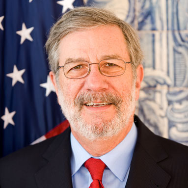 Older white man with greying hair and full beard wearing glasses and a black suit