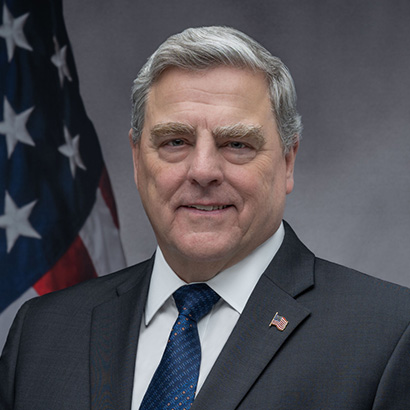 Older white man with white hair and eyebrows wearing a dark grey suit