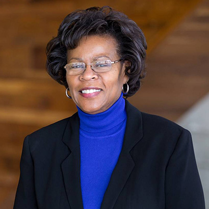 Middle-aged Black woman with fluffy bobbed hair wearing a blue turtleneck and dark blazer