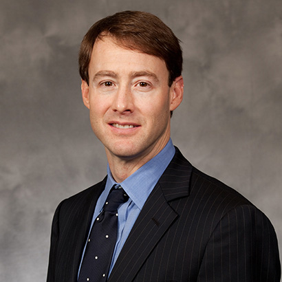 Clean-shaven white man with short brown hair wearing a black suit
