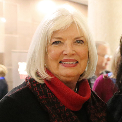 White woman with bobbed white hair wearing a red scarf and dark jacket