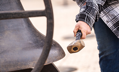 Modern photo of a closeup on a person swinging a mallet to ring a large bell
