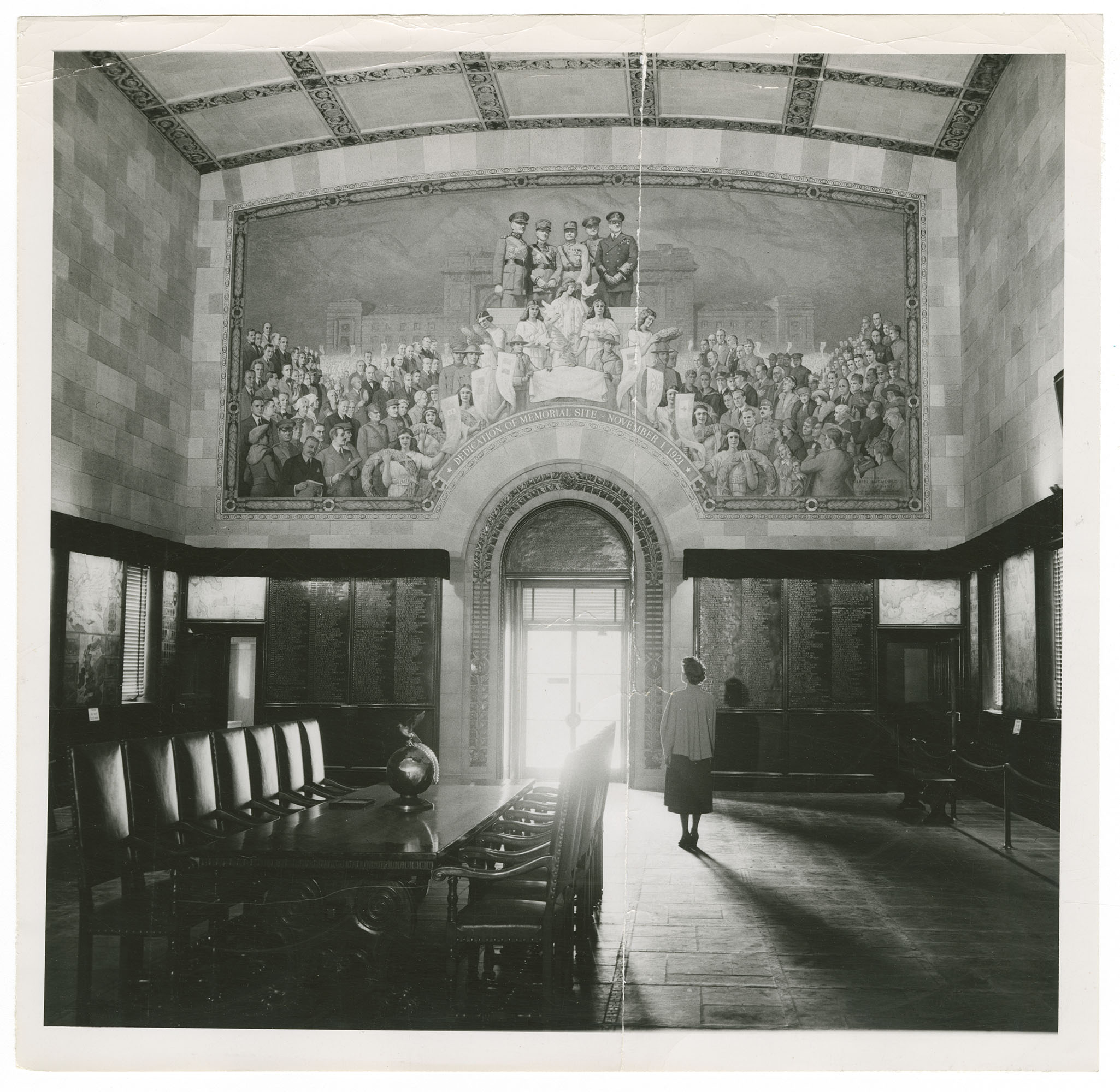 Black and white photo of the interior of Memory Hall, dominated by a painted mural of military figures on a dais surrounded by crowds.
