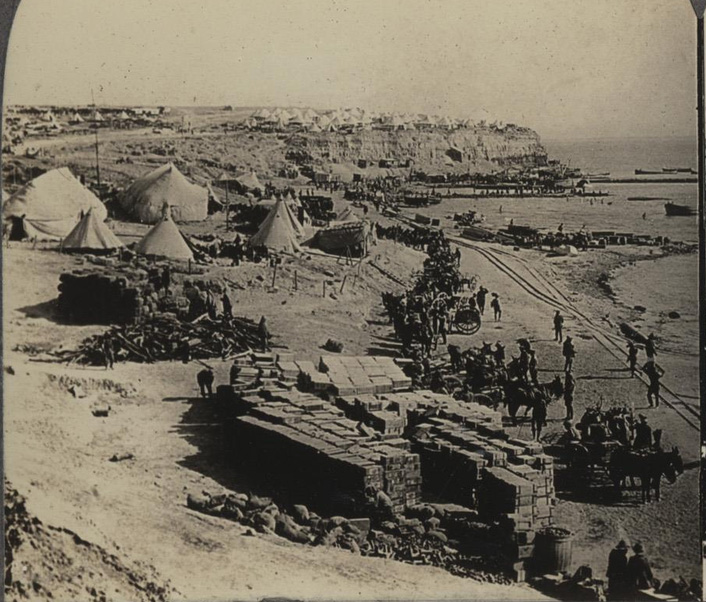 Black and white photo of a groups of soldiers, military vehicles and supplies coming onshore on a beach