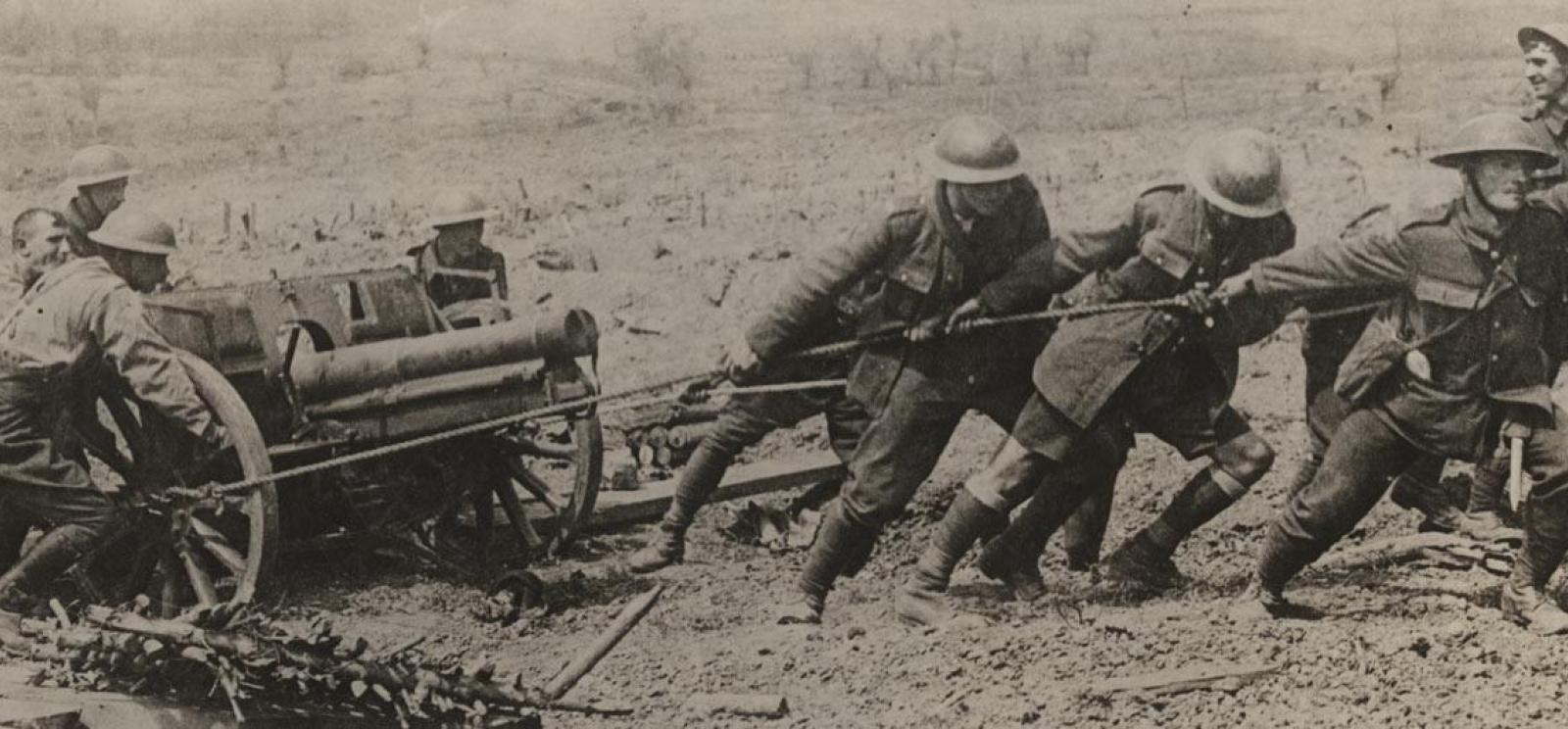 Black and white photograph of a group of men pulling and pushing a field gun.