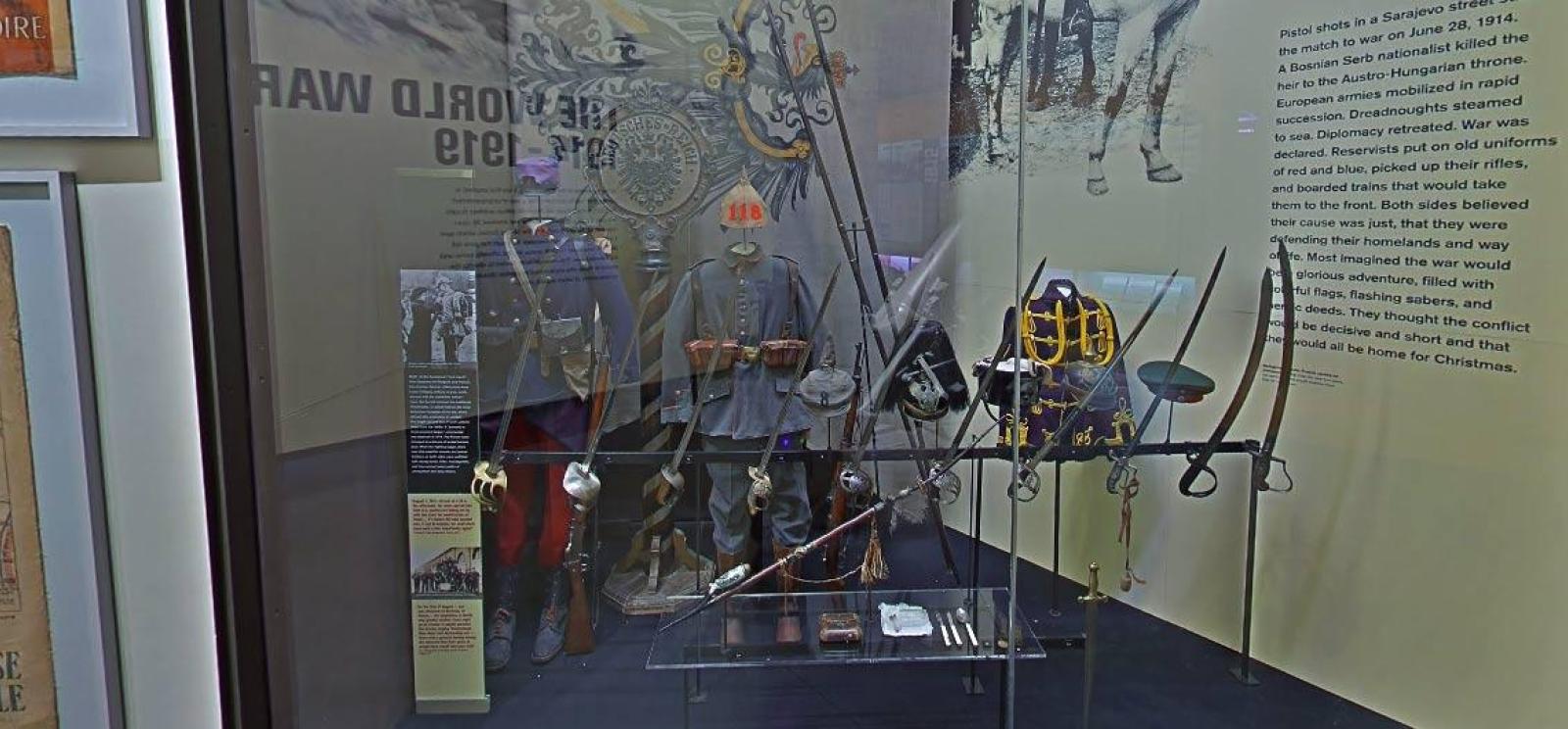 Modern photograph of a museum display of WWI-era military uniforms, hats and swords.
