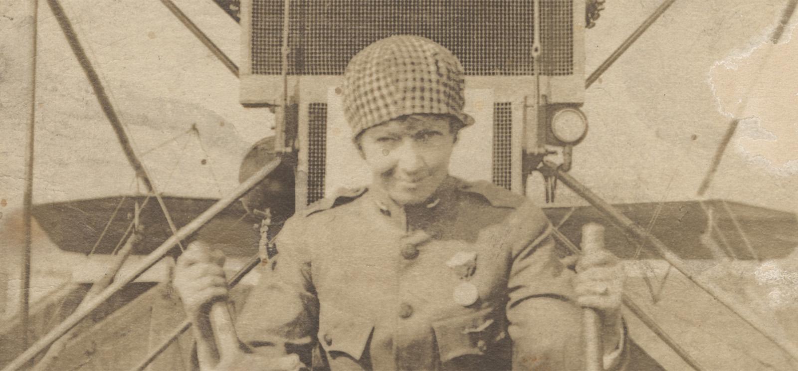 Sepia photograph of a white woman in an aviation uniform sitting in the cockpit of an WWI-era airplane