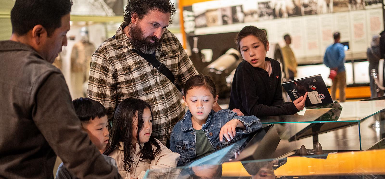 Two adults and four children gather around glass museum cases in a gallery