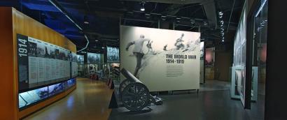 Modern photograph of the Museum main gallery. A trench gun is in the foreground. The timeline display stretches away from the viewer.