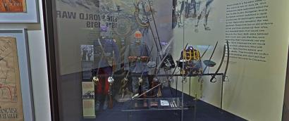 Modern photograph of a museum display of WWI-era military uniforms, hats and swords.
