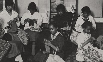 Black and white photograph of a group of Black women gathered in a room knitting various projects