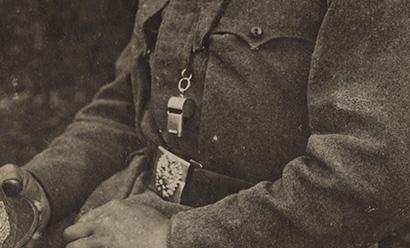 Close-up on a black and white portrait of a seated WWI officer, zoomed in on the whistle hanging on a lanyard around his neck