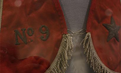 Close-up detail on a red silk stole with gold fringe trim and an embroidered star and "No. 9"