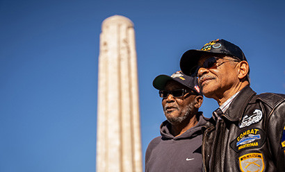 Two older Black men wearing hats and jackets embroidered with veterans patches