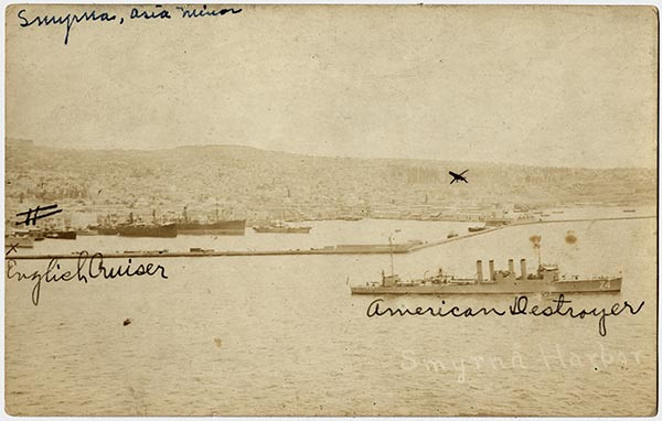 Sepia photograph of a harbor with multiple battleships in it. Two of them are labeled 'American Destroyer' and 'English Cruiser' in cursive.
