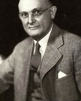 Black and white portrait photograph of a middle-aged white man wearing frameless glasses and a grey suit.