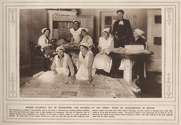 Scan of an old newspaper page. Most of the page is a large black and white photograph of a group of people sitting on the floor or in chairs over a lot of newspapers spread out on the floor.