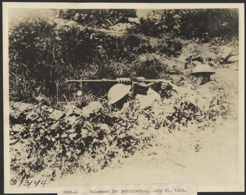 Black and white photo of several American WWI soldiers lying in a shell crater with a machine gun set up among them.