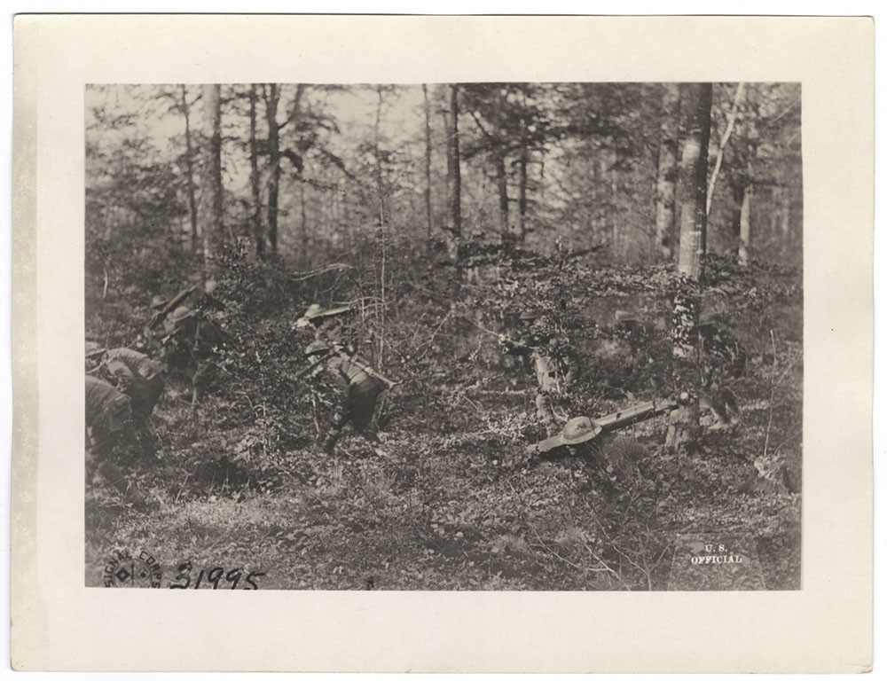 Black and white photo of American WWI soldiers moving through a forest with machine guns strapped to their backs