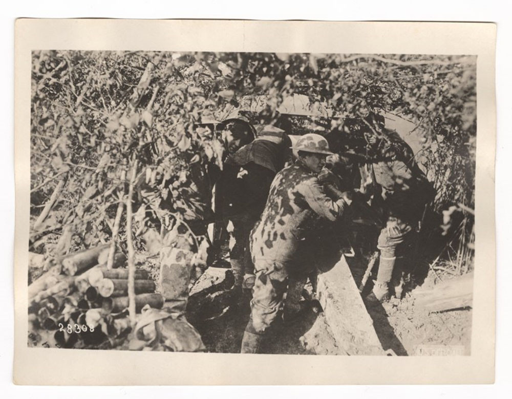 Black and white photograph. American soldiers from Battery C fire an artillery gun hidden amongst dense forest. 
